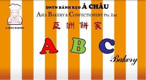 Logo cũ ABC BAKERY với màu sắc xanh đỏ bắt mắt, gắn kèm hình ảnh một cậu bé mặc đồ thợ vừa làm bánh vừa cười.